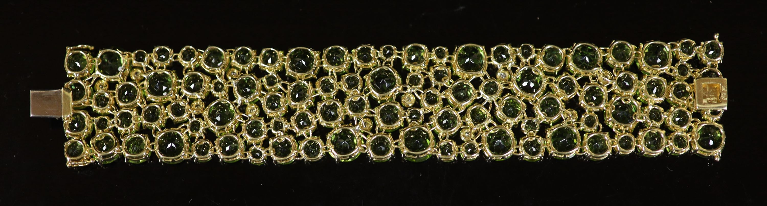 A Continental 18k gold and graduated round cut peridot encrusted bracelet, with twelve stone diamond random set spacers
